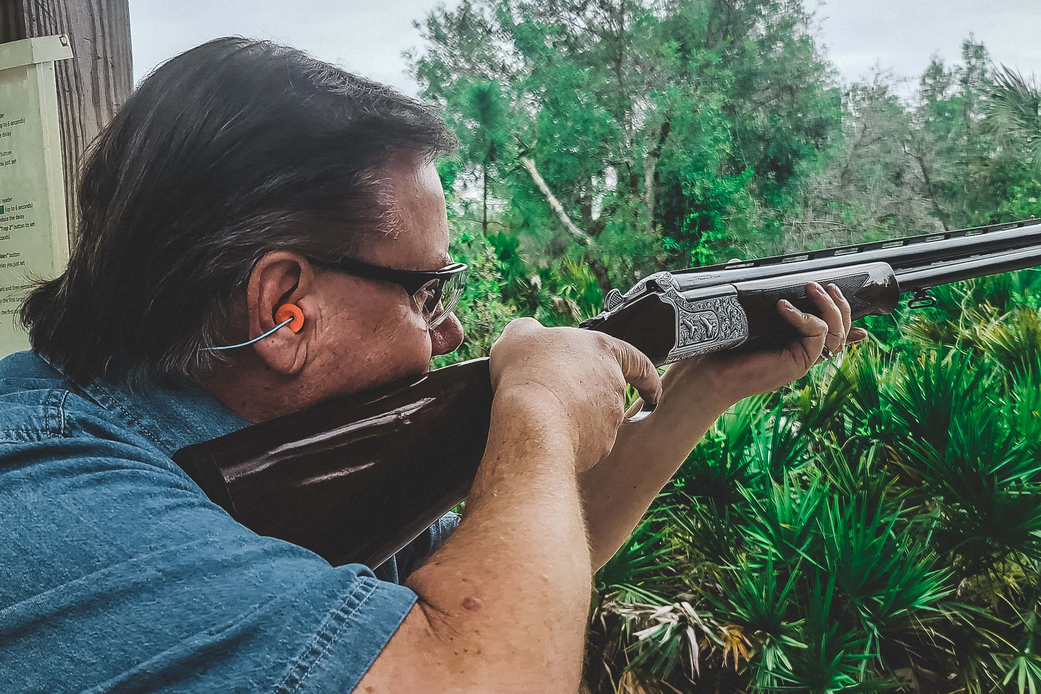 A trap shooter aiming a shotgun at a clay target